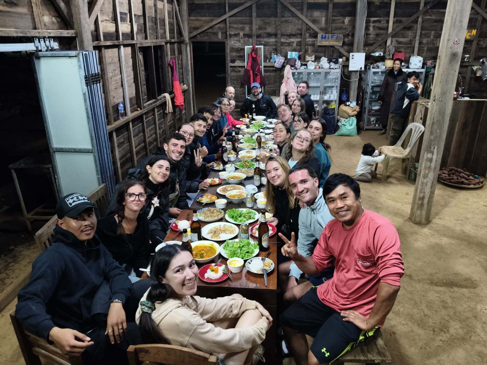 Guests enjoying a communal family dinner with fresh farm produce at wooden table on Shared Happy Farm